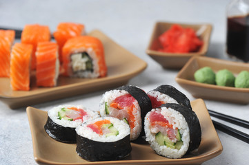 Rolls with tuna, avocado, Philadelphia cheese, fresh cucumber.  In the background soy sauce, pickled ginger and wasabi.  Light background.  Close-up.