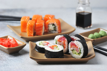 Rolls with tuna, avocado, Philadelphia cheese, fresh cucumber.  In the background soy sauce, pickled ginger and wasabi.  Light background.  Close-up.