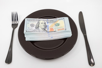 Plate full hundreds of dollar bills with fork and knife. Concept of prosperity and abundance. Full...