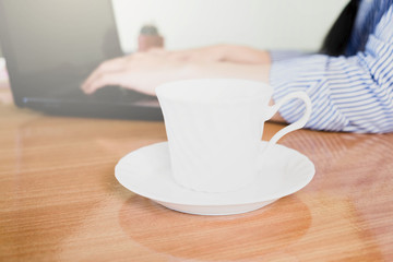 Fototapeta na wymiar selective focus white a cup of coffee and blur woman' hand wore blue striped shirt typing keybord laptop on wooden table,work online lifestyle relax at home with coffee,work from home concept
