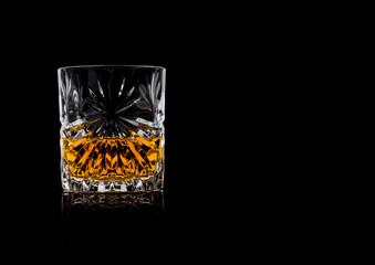 Scotch whiskey in crystal elegant glass on black background with reflection.