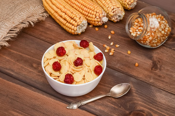 Close-up cornflakes with raspberries and ears of corn on a dark wooden background. Healthy food, breakfast
