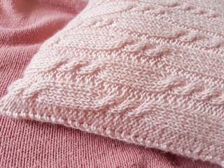 Handmade knitted cushion, soft pink pillow with cables knit stitches design on bed cover. Home decor elements