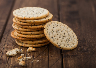 Stack of various organic crispy wheat flatbread crackers with sesame and salt on wooden background.