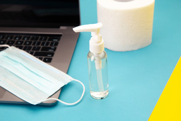 Laptop with protective face mask, chemical spray for ddisinfection and a stock of toilet paper for the days od pandemic. Quarantine concept.