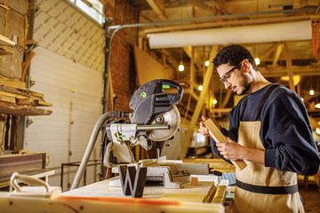 portrait of concentrated carpenter man at work place, skillful guy in uniform make furniture on an order for cutomers
