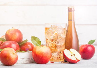 Bottle and glass of homemade organic apple cider with fresh apples in box on wooden background with sun light