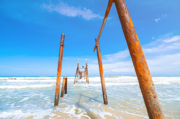 Ruins of wood bridge with beautiful wave and sky for copy space..Broken wood bridge and waves crashing on sea..Sea view from tropical beach with sunny sky. Summer paradise beach of Phuket island.