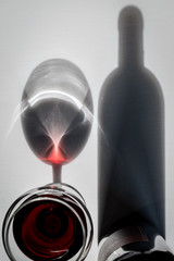 Glass of red wine and bottle with shadows and reflections on a white textured surface. High angle view.