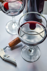Closeup of glasses of red wine and bottle with shadows and reflections on a white textured surface.