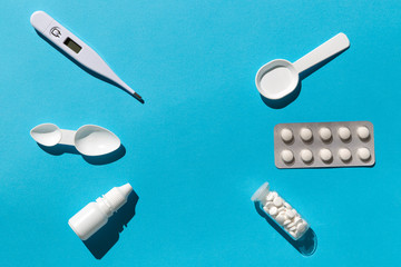Medical treatment kit flat lay with copy space in the middle. Medicines, pills, thermometer, supplement, nasal drops on blue background.