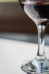 Closeup of glasses of red wine and bottle with shadows and reflections on a white textured surface.
