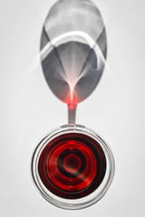Closeup top view of a glass of red wine with shadows and reflections on a white textured surface.