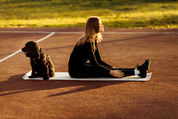 Athlete young girl during doing sports exercises with hblack pretty dog outdoors on the stadium .
