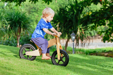 2 - 3 years joyful boy riding a wooden balance bike (run bike). Happy barefoot child learning to...
