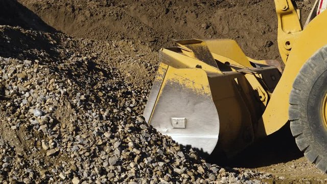 Loader filling its bucket in slow motion. Huge rubber wheel compresses under the pressure of bucket being loaded.