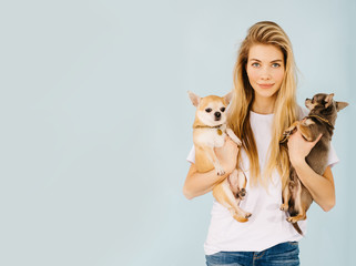 beautiful blonde girl holding a little dog on a blue background place for text
