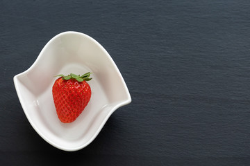 Strawberry in white bowl on a dark slate desk. There is enough space in the photo for your use.