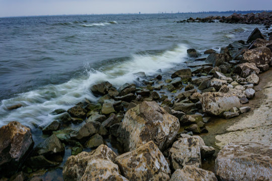 Landscape with waves crashing against the coastal stones at sunrise.