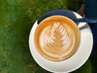 Cup of Cappuccino with a leaf shaped foam on a glass table in a garden