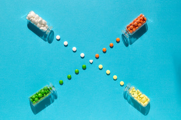 Colorful, orange, green, yellow, white pills spill out of the transparent bottle to the middle into heart shaped pill. Medical flat lay with pill  on the blue background. Improve your immunity concept