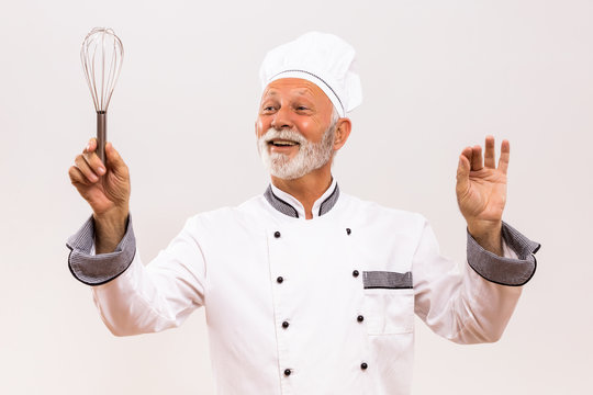 Image of  musical conductor senior chef with wire whisk on gray background.