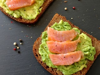Avocado toasts with slices of smoked salmon and pepper on the dark backround, top view