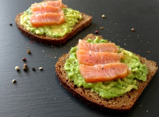 Avocado toasts with slices of smoked salmon and pepper on the dark backround