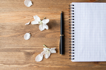 Notepad with a blank sheet of paper and pen on a wooden background with delicate flowers of an apple tree