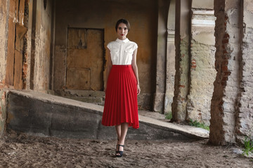 Fashion Model Girl with brown hair against the background of an old, abandoned building in a stylish red skirt and shirt