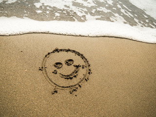 smiley written in beach sand with blue ocean water foam in the background 