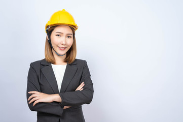 Portrait of Young Asian businesswoman wearing yellow safety-helmet in formal suit smiling looking at camera, shot in studio
