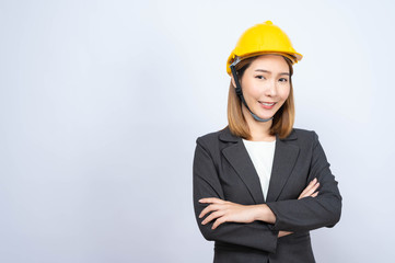 Portrait of Young Asian businesswoman wearing yellow safety-helmet in formal suit smiling looking at camera, shot in studio