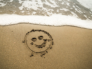 smiley written in beach sand with blue ocean water foam in the background 