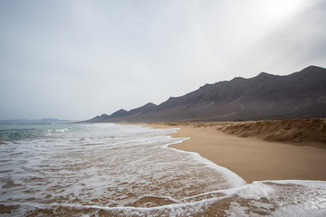 
orilla del mar con arena y olas en el fondo el horizonte entre el mar y el cielo azul.