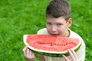 the boy holds a slice of red watermelon and wants to bite off a slice, looking forward