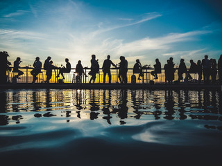 silhouette of people at a after work pool party in the sunset with light reflecting in the blue...