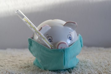 Piggy bank with the thermometer in respirator mask presenting the economics issues and financial...