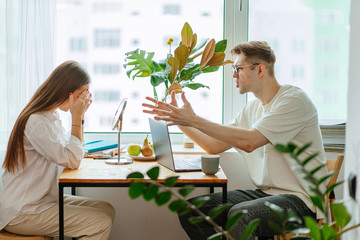 young caucasian woman prevents her husband from working at home, man sit with laptop and yelling at...