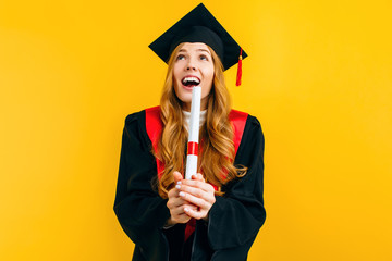 Excited beautiful graduate, with a diploma on a yellow background. Concept of the graduation...