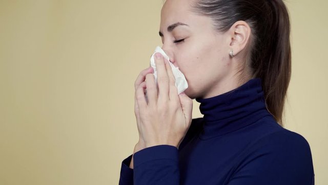 Portrait of young woman blows her nose into napkin, sneezes and coughs, isolated
