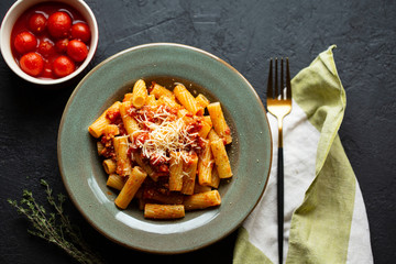 Tasty appetizing classic Italian pasta with tomato sauce, parmesan cheese and noodles on a plate on a dark table.Top view, horizontal.Italian pasta.Penne pasta in tomato sauce with chicken, tomatoes.