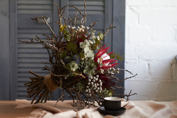 Cup of coffee and exotic bouquet without packaging stands on table with beige linen tablecloth, holiday morning concept, selective focus