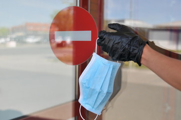 Hand with glove holding face mask in front of forbidden entry sign