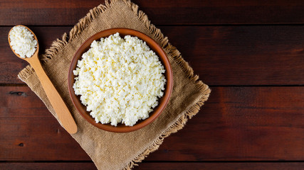 Cottage cheese on wooden boards. Fresh cottage cheese in a ceramic bowl. Soft cheese and wooden spoon on a burlap. Top view. Copy space