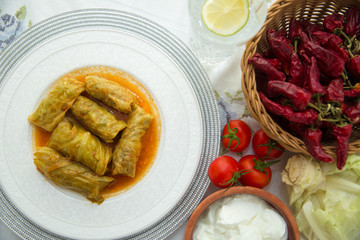Meat stuffed cabbage leaves, stewed in tomato sauce . Cabbage stuffing on a white plate . Red pepper in the basket. Red tomatoes and cabbage. Yogurt in a brown bowl .