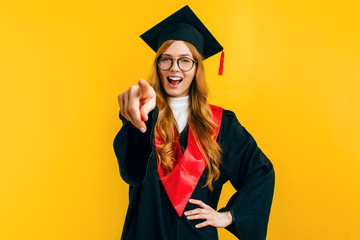 A happy graduate in a graduation cap, pointing at the camera with her index finger and smiling...