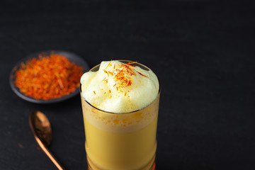 Saffron latte in a glass cup on concrete background,metal straw,dry spice saffron