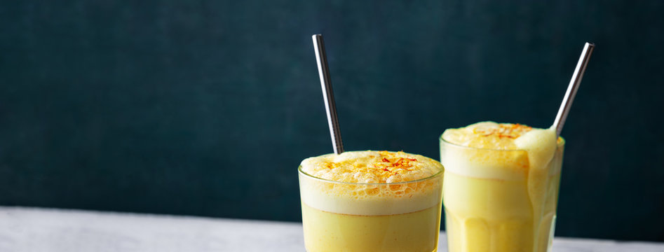 Saffron latte in a glass cup on concrete background,metal straw,dry spice saffron