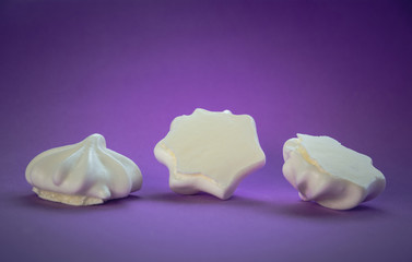 Fototapeta na wymiar Three white meringues lie on a lilac background with a vignetting effect